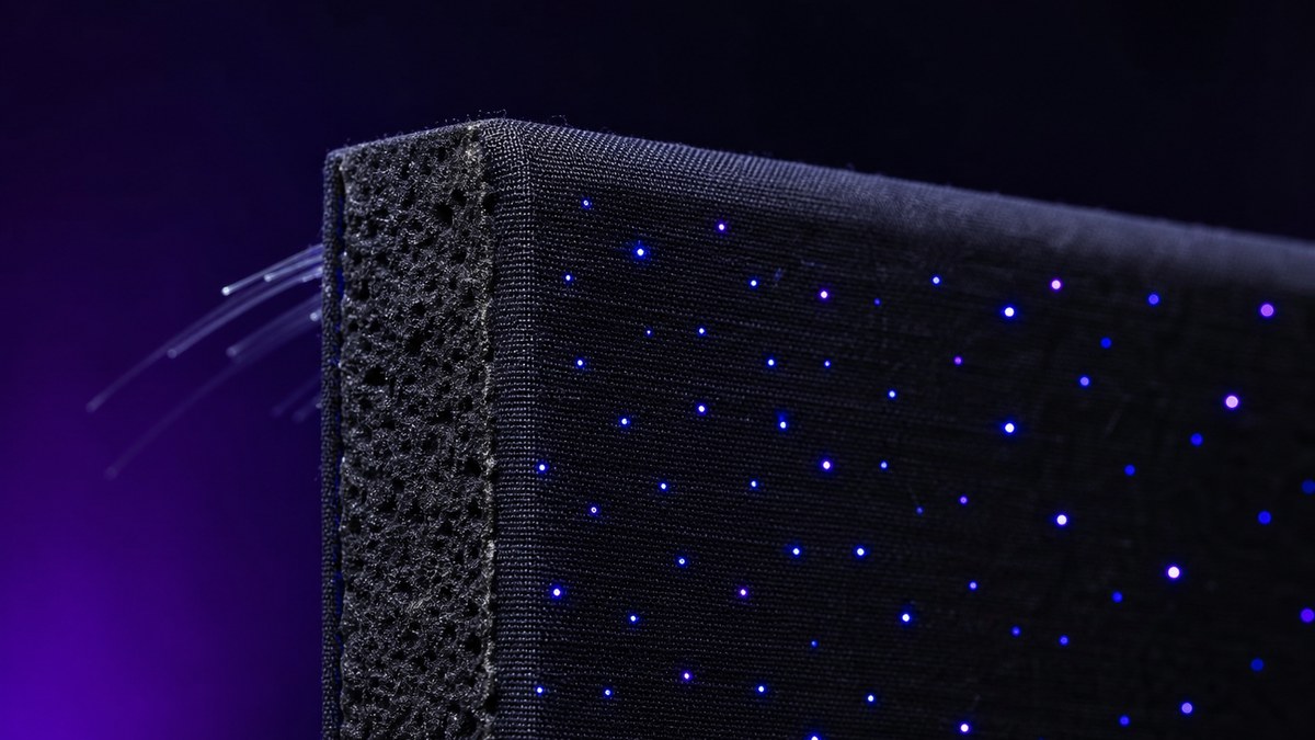 Close-up edge of a black fabric-wrapped acoustic star ceiling panel showing the thick sound-absorbing core and fiber optic strands