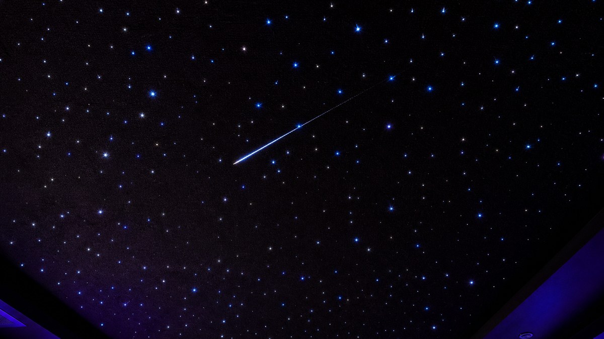 Close-up of a shooting star effect streaking across a custom fiber optic star ceiling with twinkling stars in a dark room