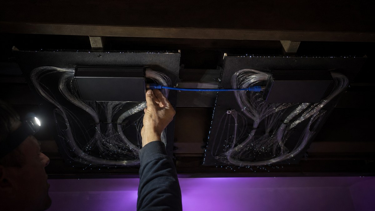 Installer connecting a blue low-voltage Cat5 cable between the light engines of two fiber optic star ceiling panels during installation