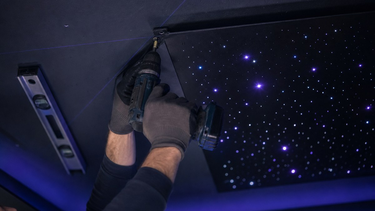 Close-up of an installer fastening a premade star ceiling panel to a drywall ceiling with mounting hardware during starlight ceiling installation